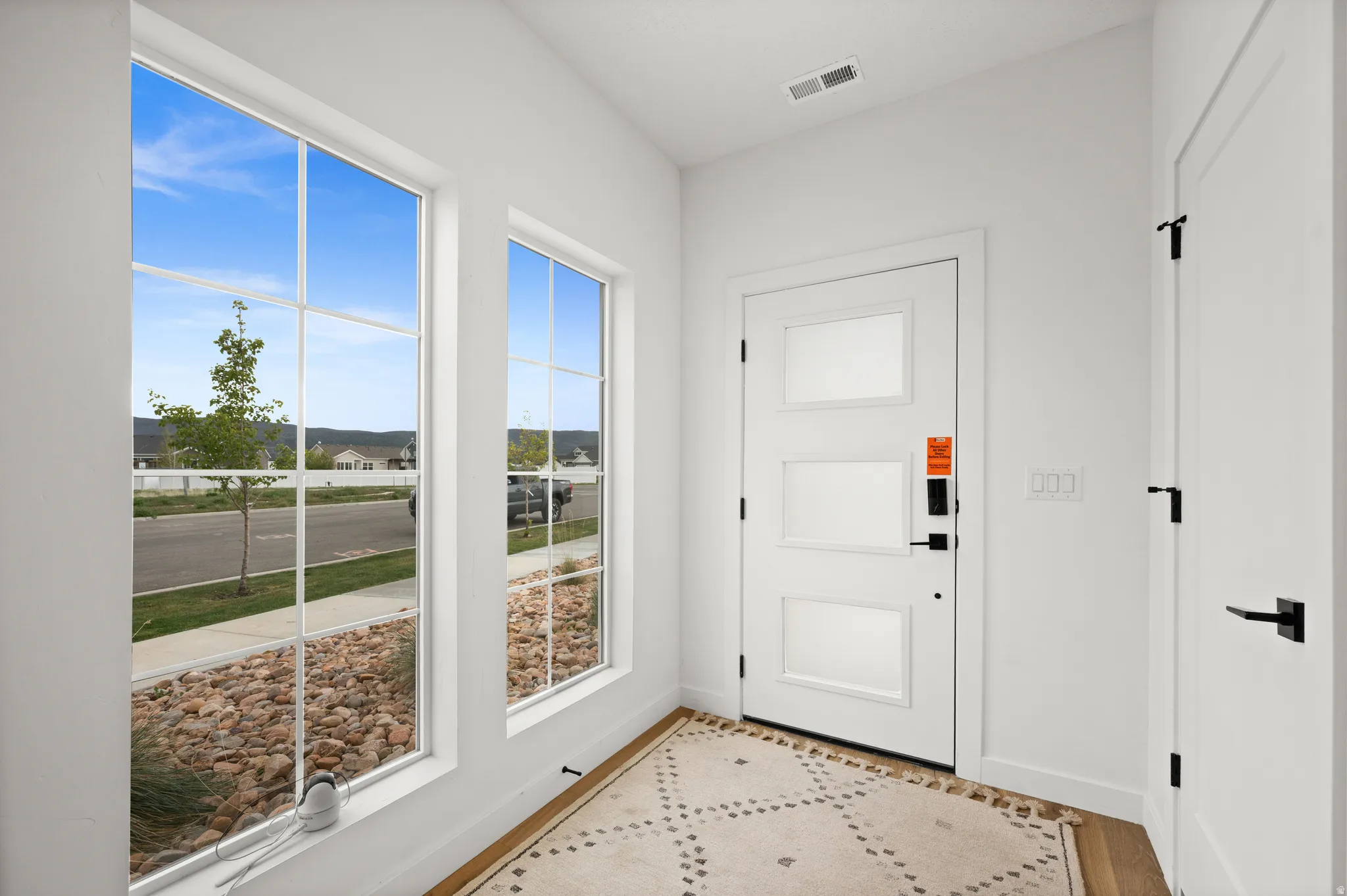 Entryway featuring a white door with frosted glass panels and matte black hardware, two large multi-pane windows, light wood-finish flooring, and white walls