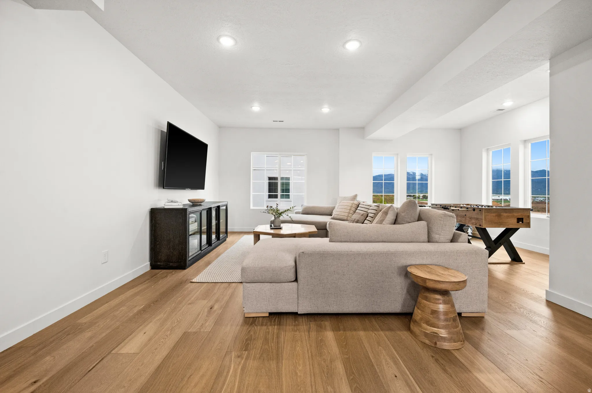 Spacious interior room featuring light wood-finish flooring, recessed lighting, and multiple windows offering expansive mountain scenery