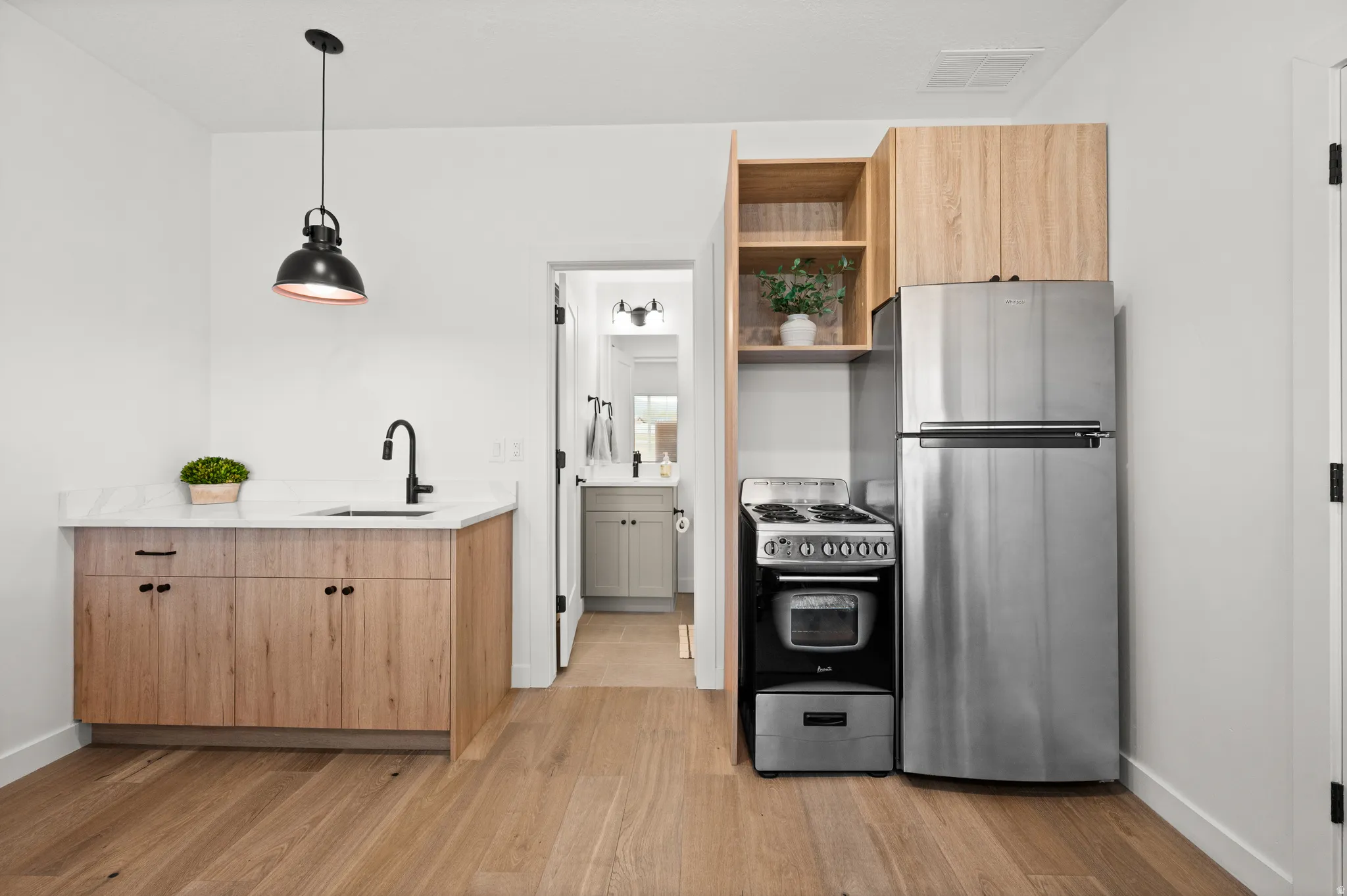 Efficient kitchen area featuring wood-finish flooring, light wood cabinetry, white stone-finish countertops, and a black gooseneck faucet
