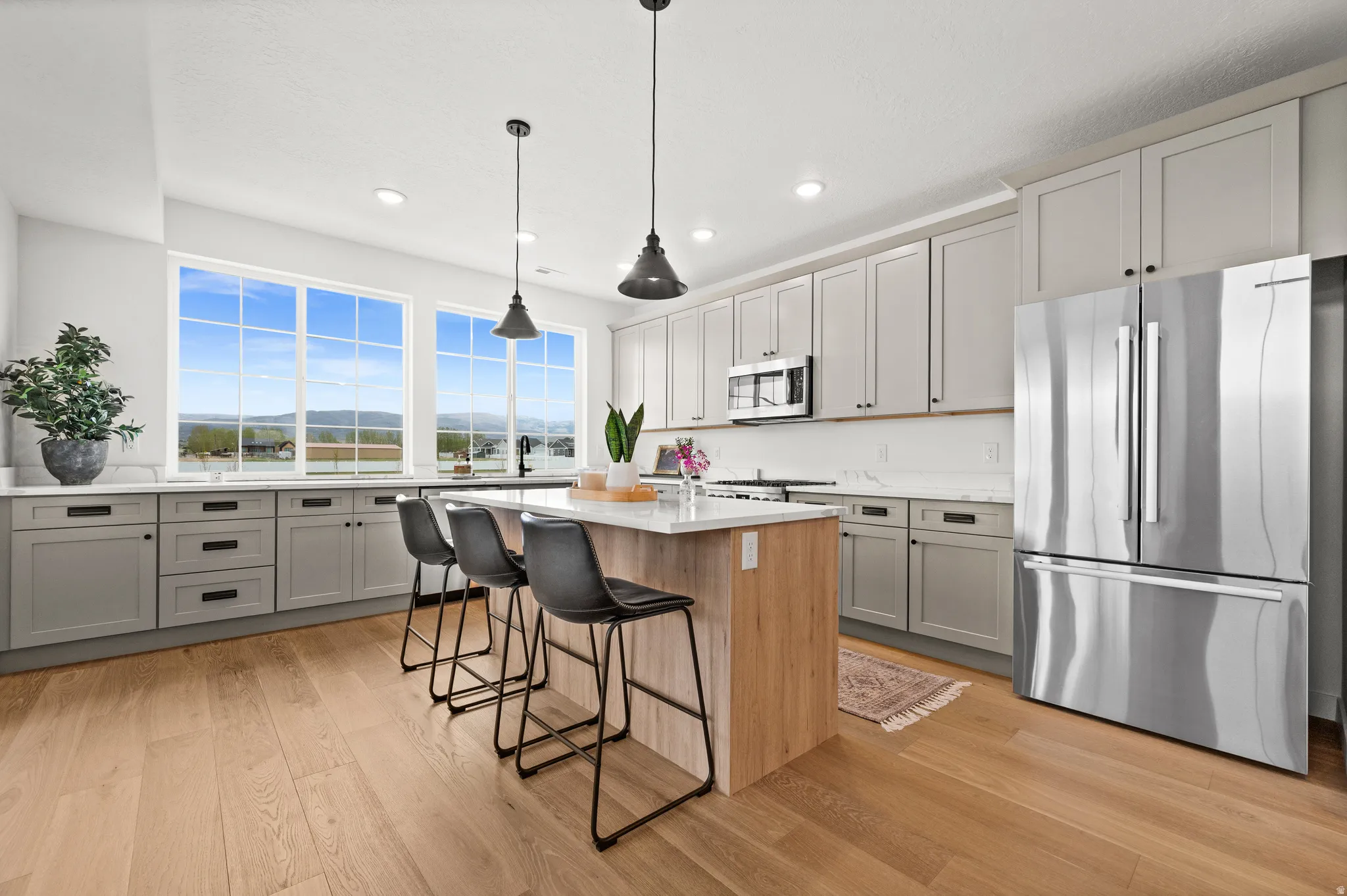 Bright kitchen featuring light wood-finish flooring, a central island with white countertop, grey cabinetry, stainless steel appliances, and large picture windows
