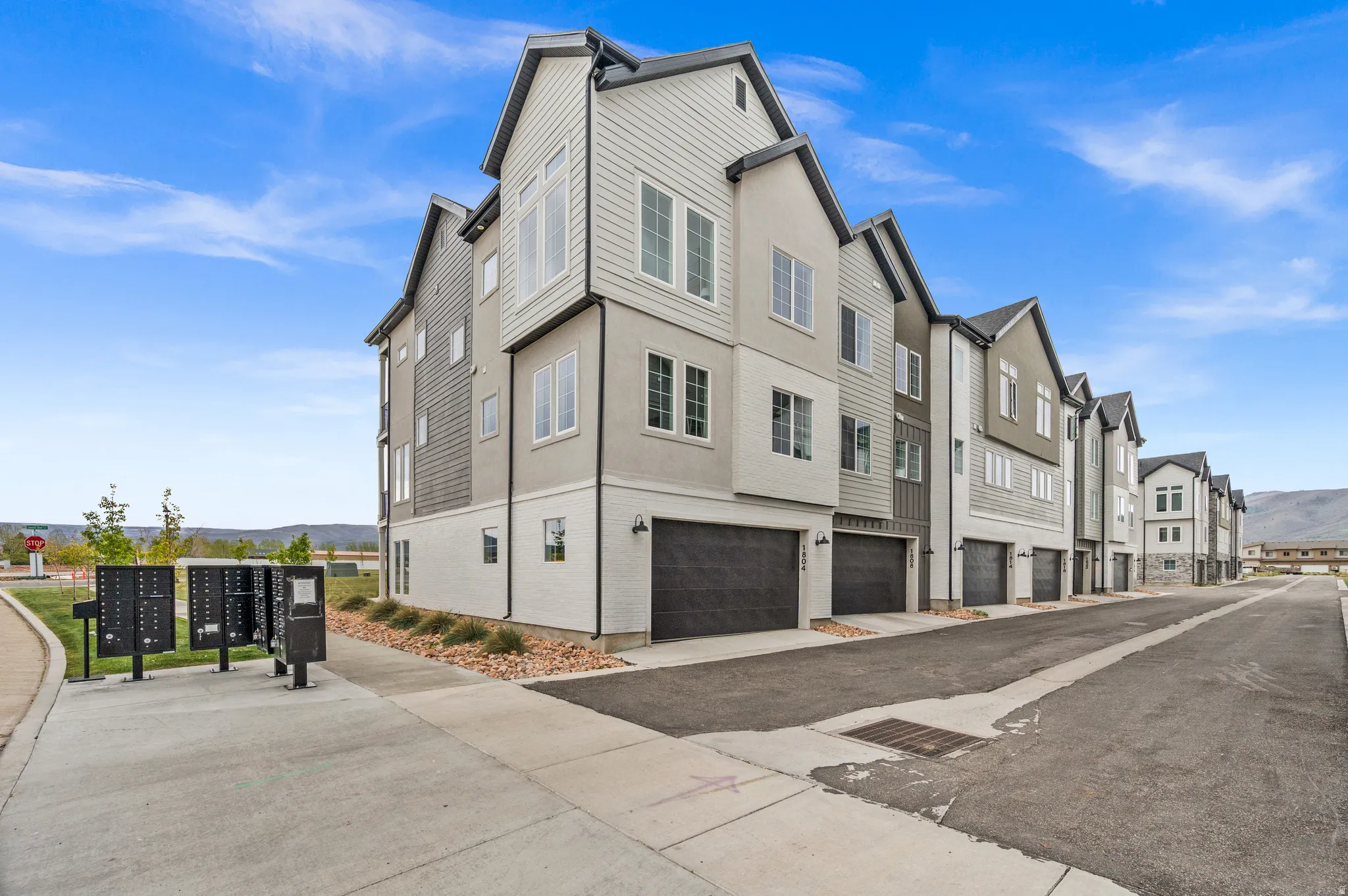 Modern townhome exterior featuring multi-level architecture, a two-car garage, and a light-colored stucco and siding facade
