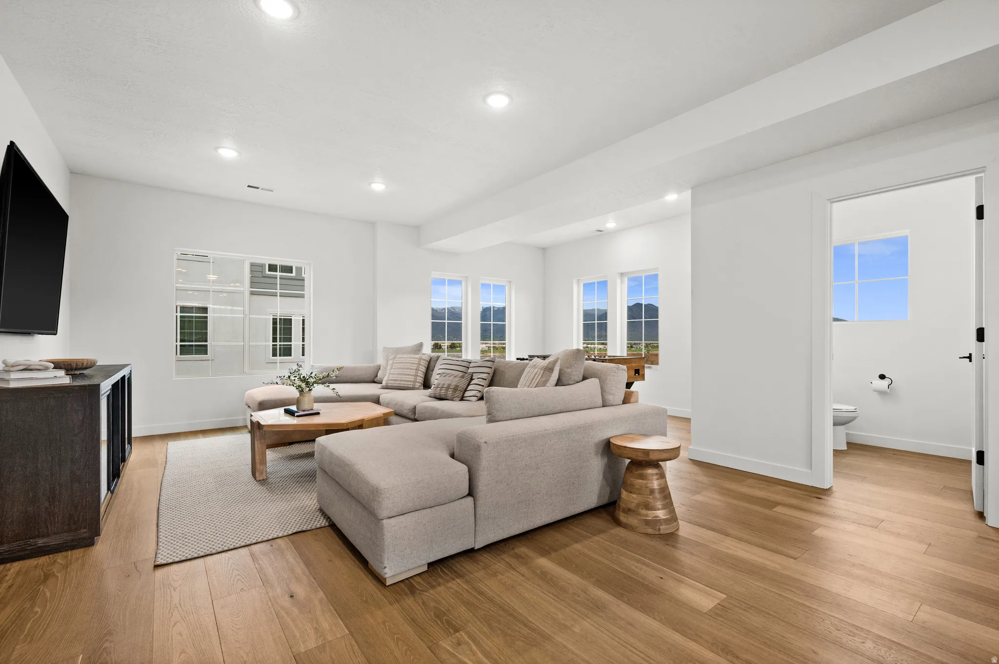 Spacious living area featuring light wood-finish flooring, recessed lighting, and multiple windows