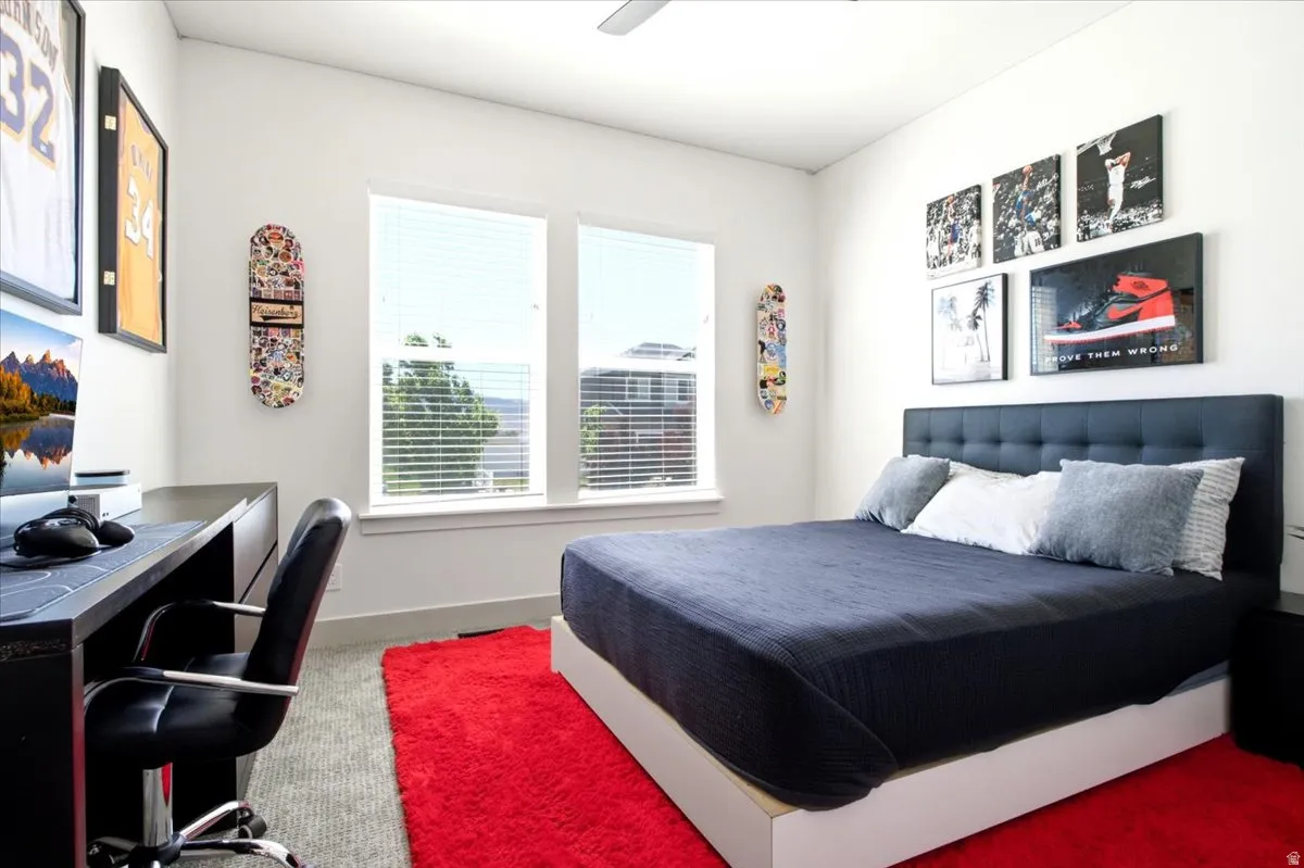 Bedroom featuring dual windows with blinds, a built-in dark wood-finish desk, a ceiling fan, and a paneled accent wall