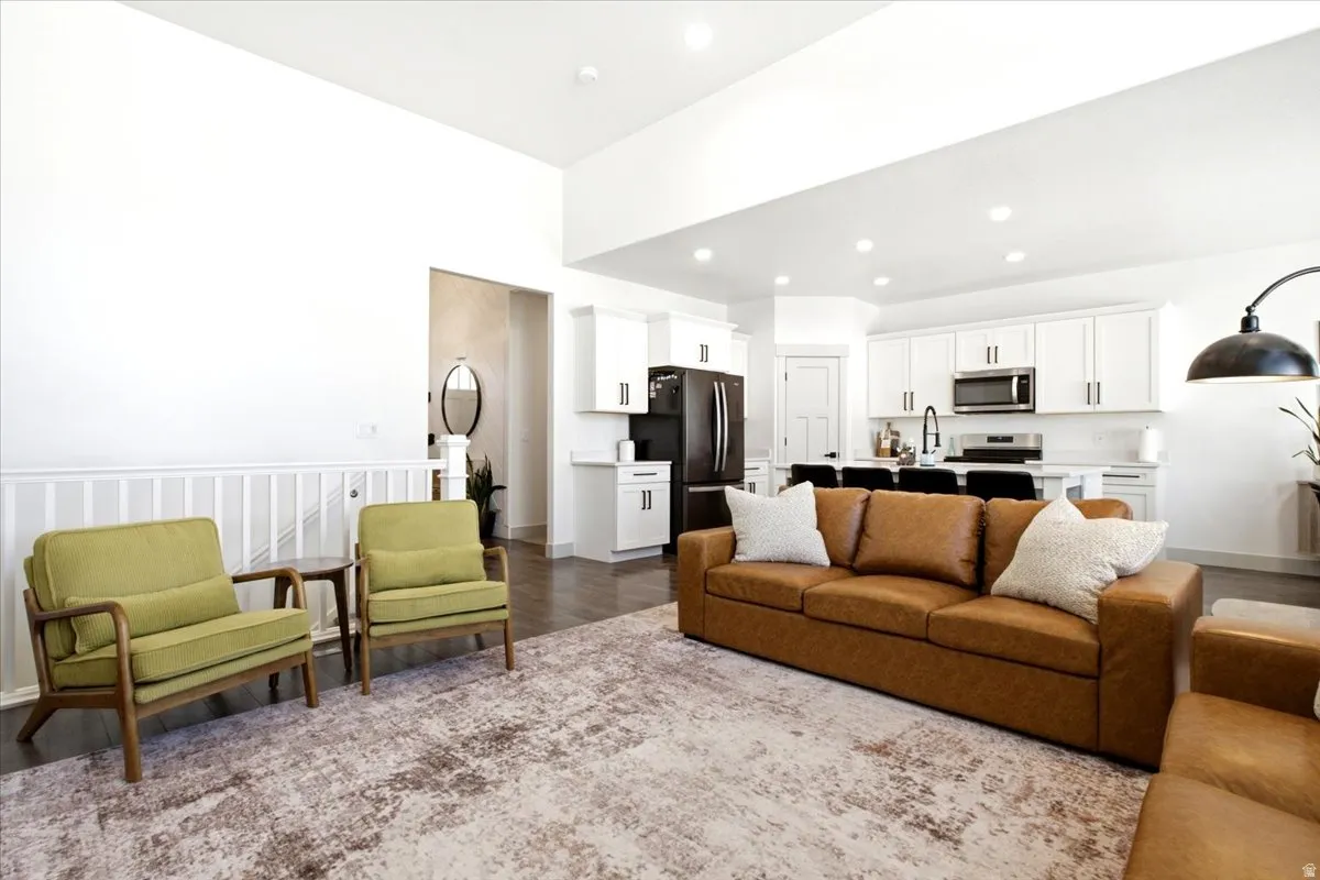 Open-concept living area featuring high ceilings, dark wood-finish flooring, white kitchen cabinetry with dark hardware, stainless steel kitchen appliances, and recessed lighting