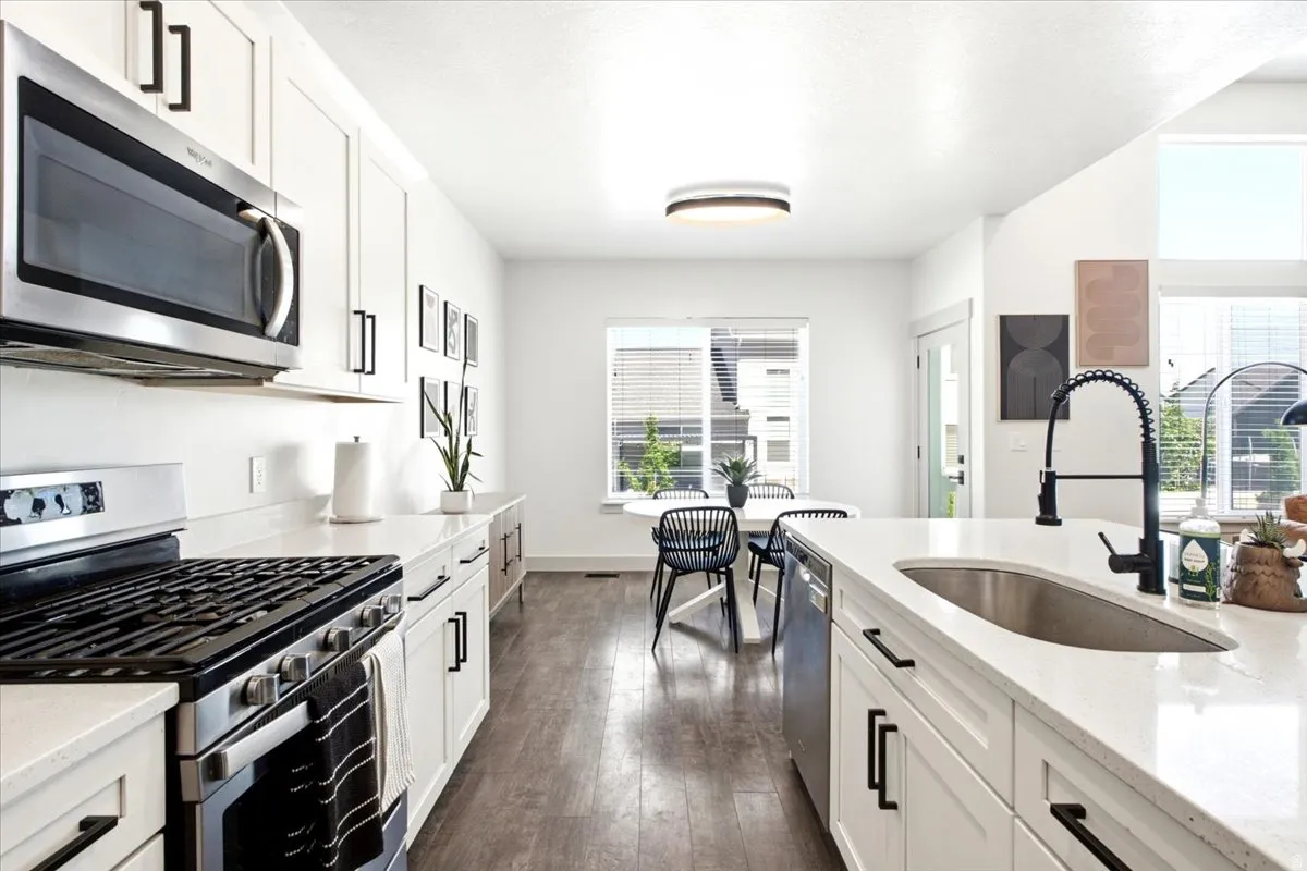 Modern kitchen featuring white cabinetry, light-toned countertops, stainless steel appliances, wood-finish flooring, and a stainless steel undermount sink with a matte black faucet