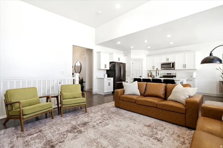 Open-concept living area featuring high ceilings, dark wood-finish flooring, white kitchen cabinetry with dark hardware, stainless steel kitchen appliances, and recessed lighting