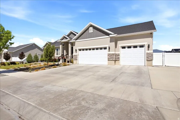 Contemporary stucco exterior with a two-car garage, stone accents, a deep concrete driveway, and established front landscaping