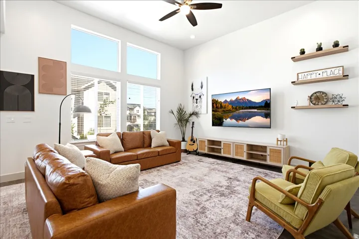 Spacious living area featuring high ceilings, large windows with blinds, a ceiling fan, light wood-finish flooring, and a built-in media console