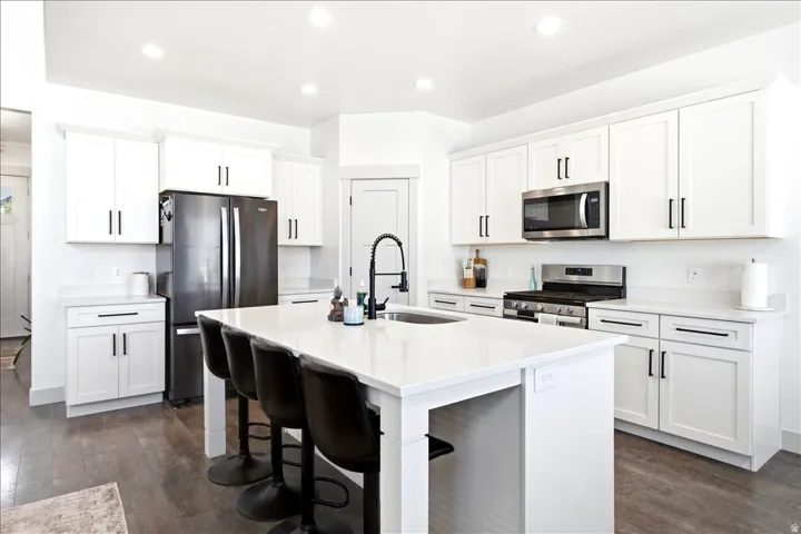 Modern kitchen featuring a large central island with seating, white shaker-style cabinetry, stainless steel appliances, and wood-finish flooring