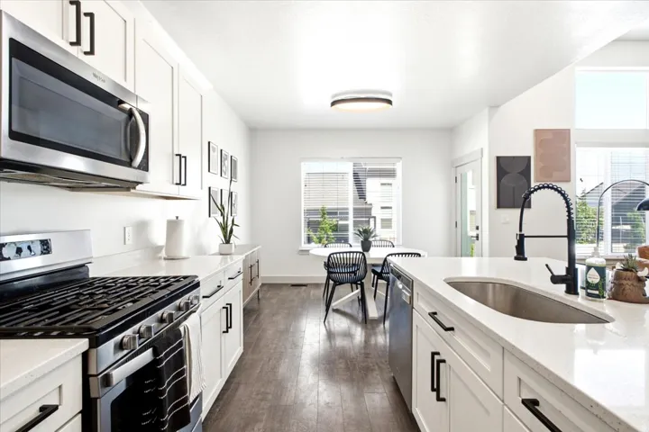 Modern kitchen featuring white cabinetry, light-toned countertops, stainless steel appliances, wood-finish flooring, and a stainless steel undermount sink with a matte black faucet