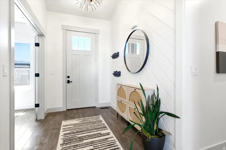 Inviting entryway with a white paneled front door, overhead light fixture, wood-finish flooring, and shiplap accent wall