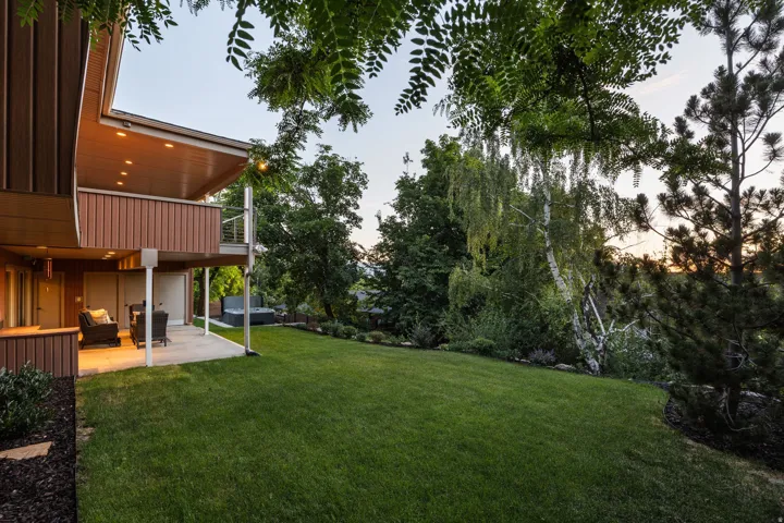 Expansive backyard featuring a manicured lawn, established landscaping, and mature trees