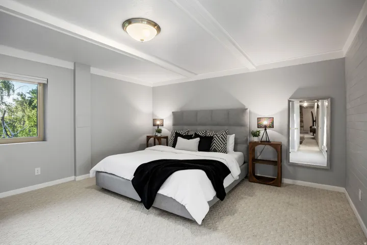 Bedroom featuring textured light gray walls, an upholstered headboard, a window with a roller shade, and an overhead flush-mount light fixture