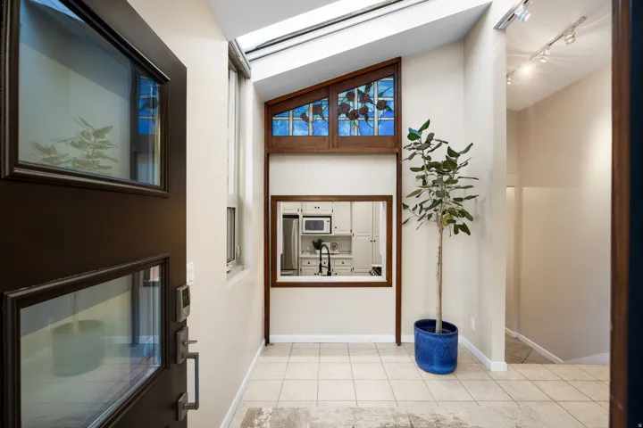 Foyer featuring tile flooring, a dark wood-framed window looking into the kitchen, a skylight, and a decorative stained glass window with wood trim