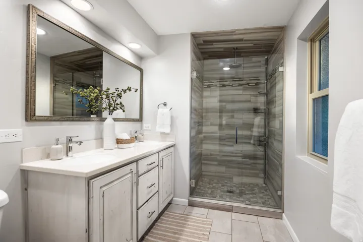 Glass-enclosed shower featuring a rain shower head, horizontal tile work, and pebble-style floor