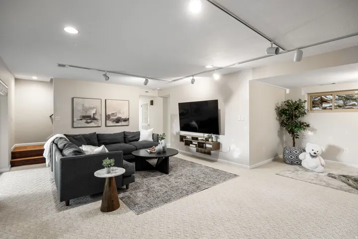 Spacious recreation room featuring patterned carpeting, recessed lighting, track lighting, and a built-in window with wood trim