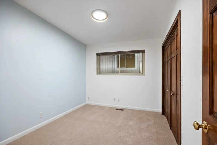 Room featuring a neutral carpet, a light blue accent wall, white painted walls, a window with a wood frame, and a flush-mount ceiling light fixture
