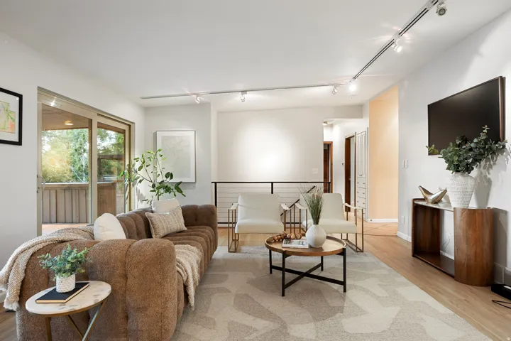 Bright living area featuring wood-finish flooring, sliding glass doors to an outdoor deck, a black metal railing, and recessed track lighting