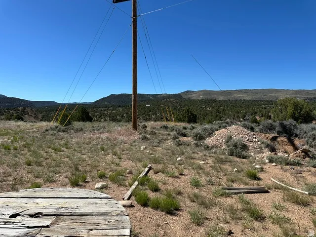 Expansive undeveloped land featuring a utility pole, overhead lines, scattered rocks, and distant hills with natural vegetation