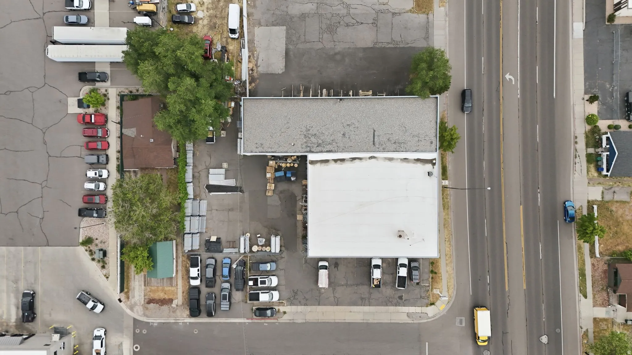 Commercial property featuring a large structure with a flat roof, an adjacent smaller building with a gabled roof, and extensive paved areas