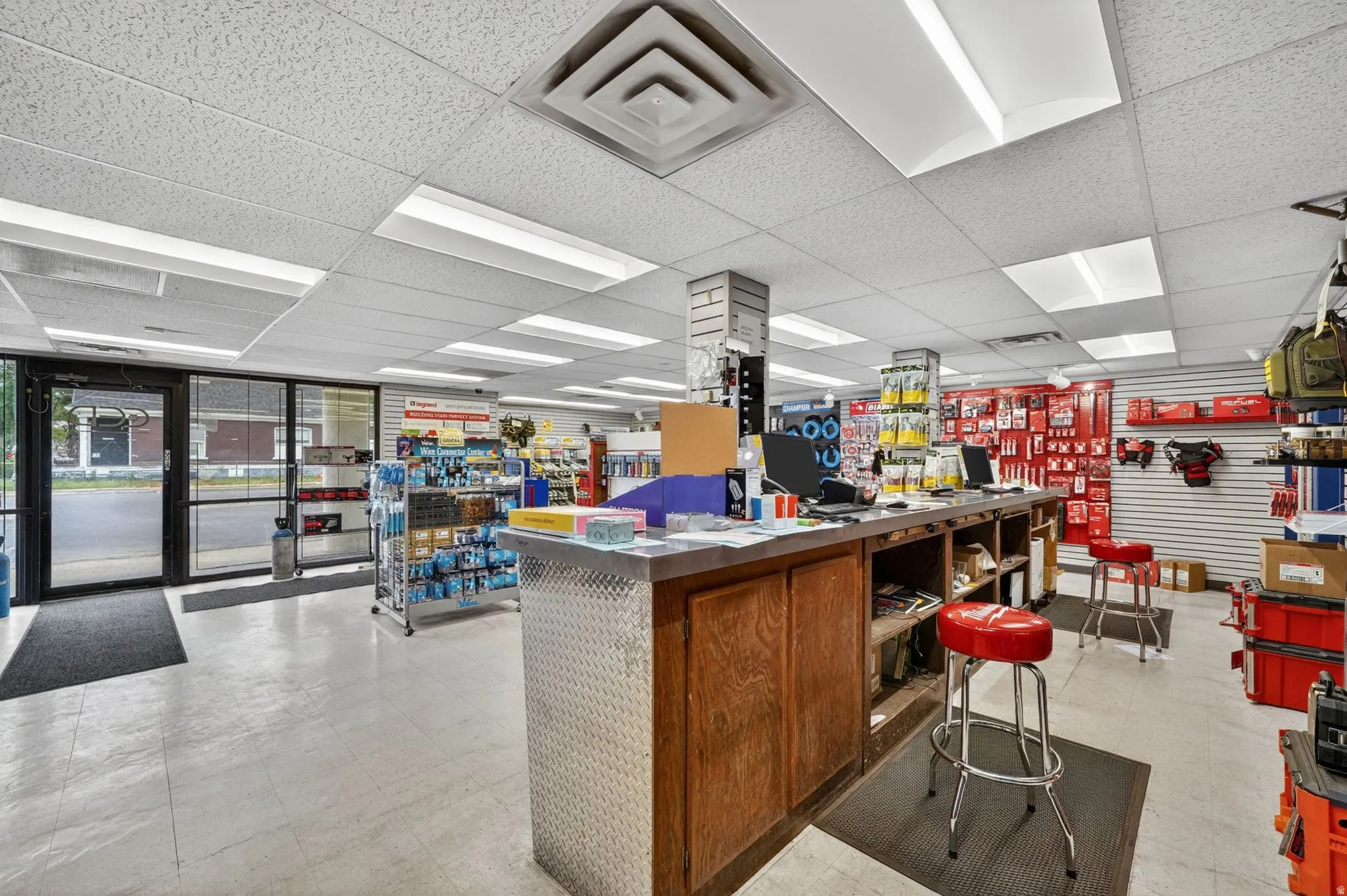 Retail storefront featuring a glass entry, suspended acoustic ceiling, recessed fluorescent lighting, and a service counter with a diamond plate facade