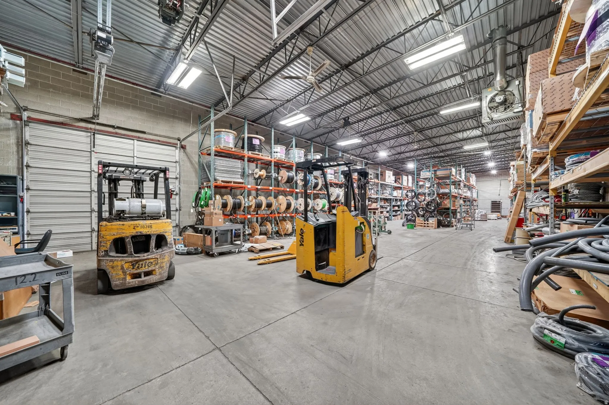Spacious warehouse interior featuring a concrete floor, high ceilings with exposed metal trusses, and fluorescent strip lighting