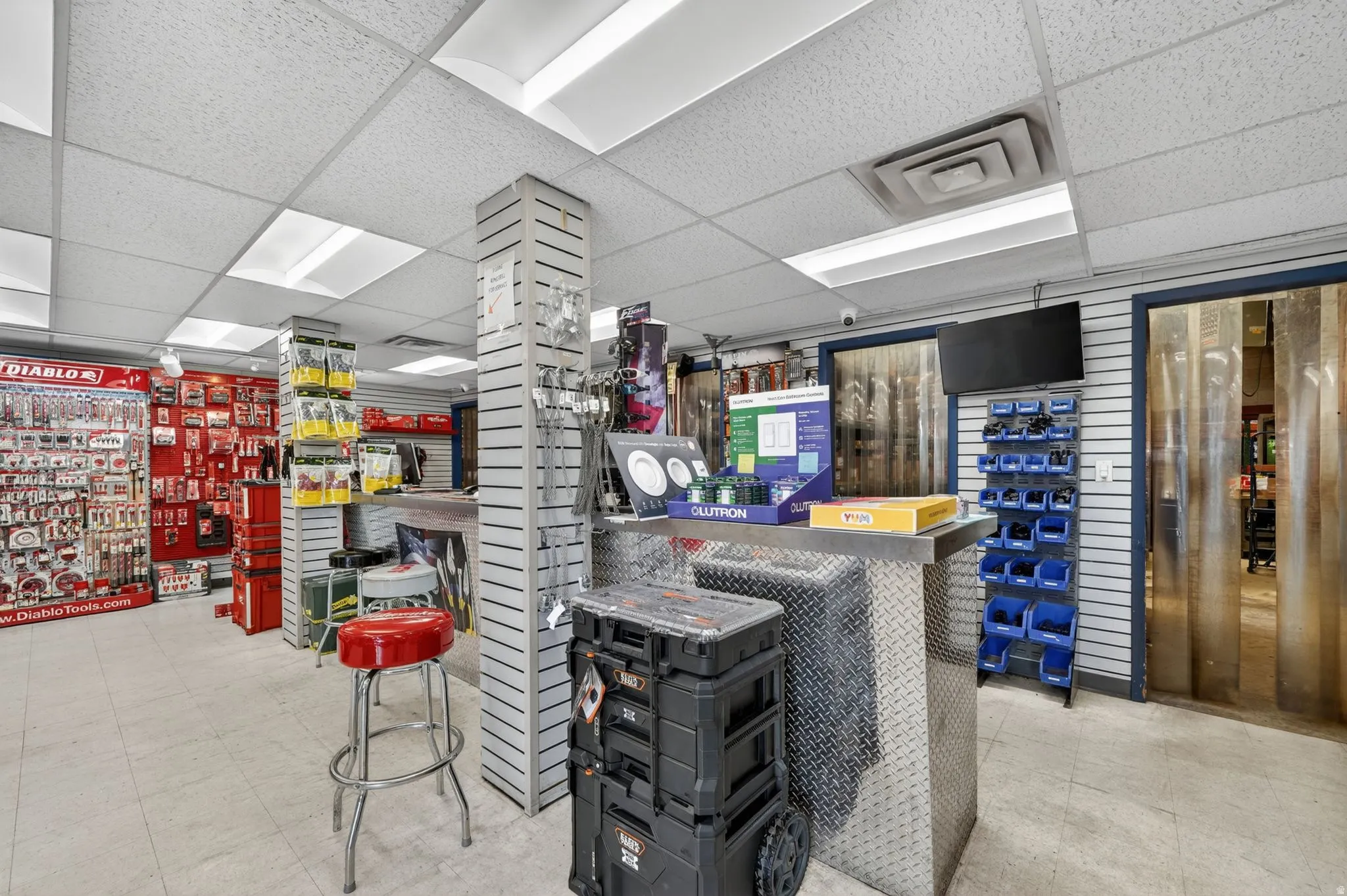 Retail interior featuring commercial-grade tile flooring, suspended acoustic ceiling tiles with integrated fluorescent lighting, slatwall paneling, and a diamond plate counter