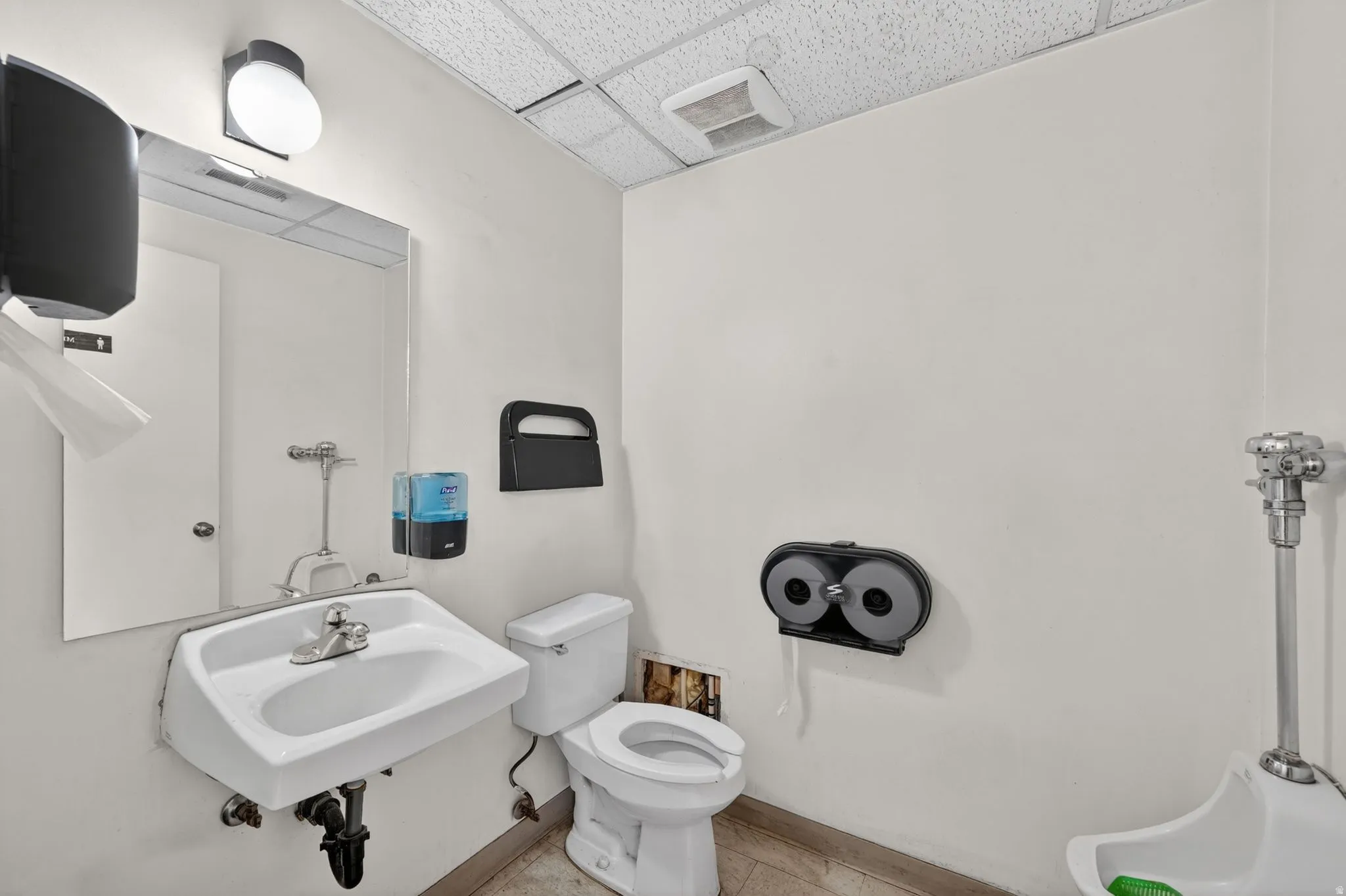 Restroom featuring a wall-mounted sink with chrome fixtures, a toilet, and a urinal