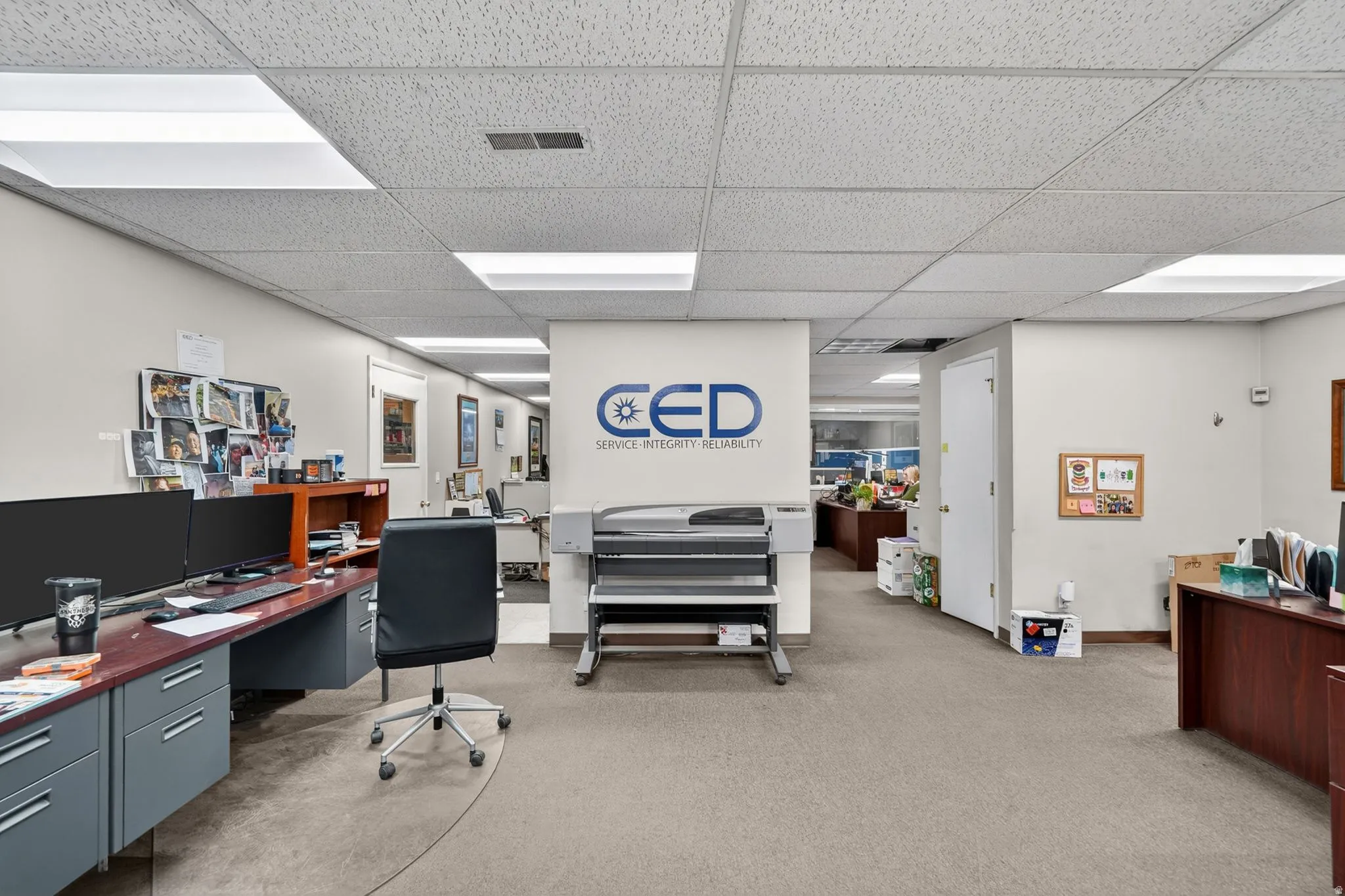 Open office area featuring suspended acoustic ceiling tiles with integrated fluorescent lighting, neutral wall finishes, and carpeted flooring