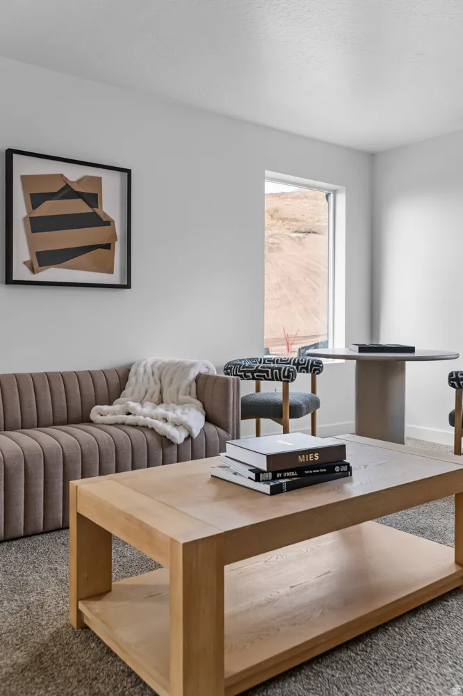 Bright interior space featuring a window with natural light, light-colored carpeting, and a framed abstract wall art piece
