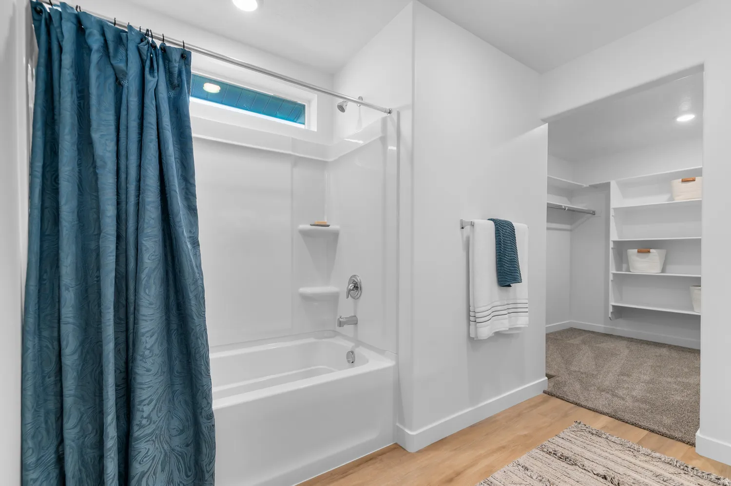 White bathtub and shower combination with chrome fixtures, a horizontal transom window, and adjacent walk-in closet with built-in shelving