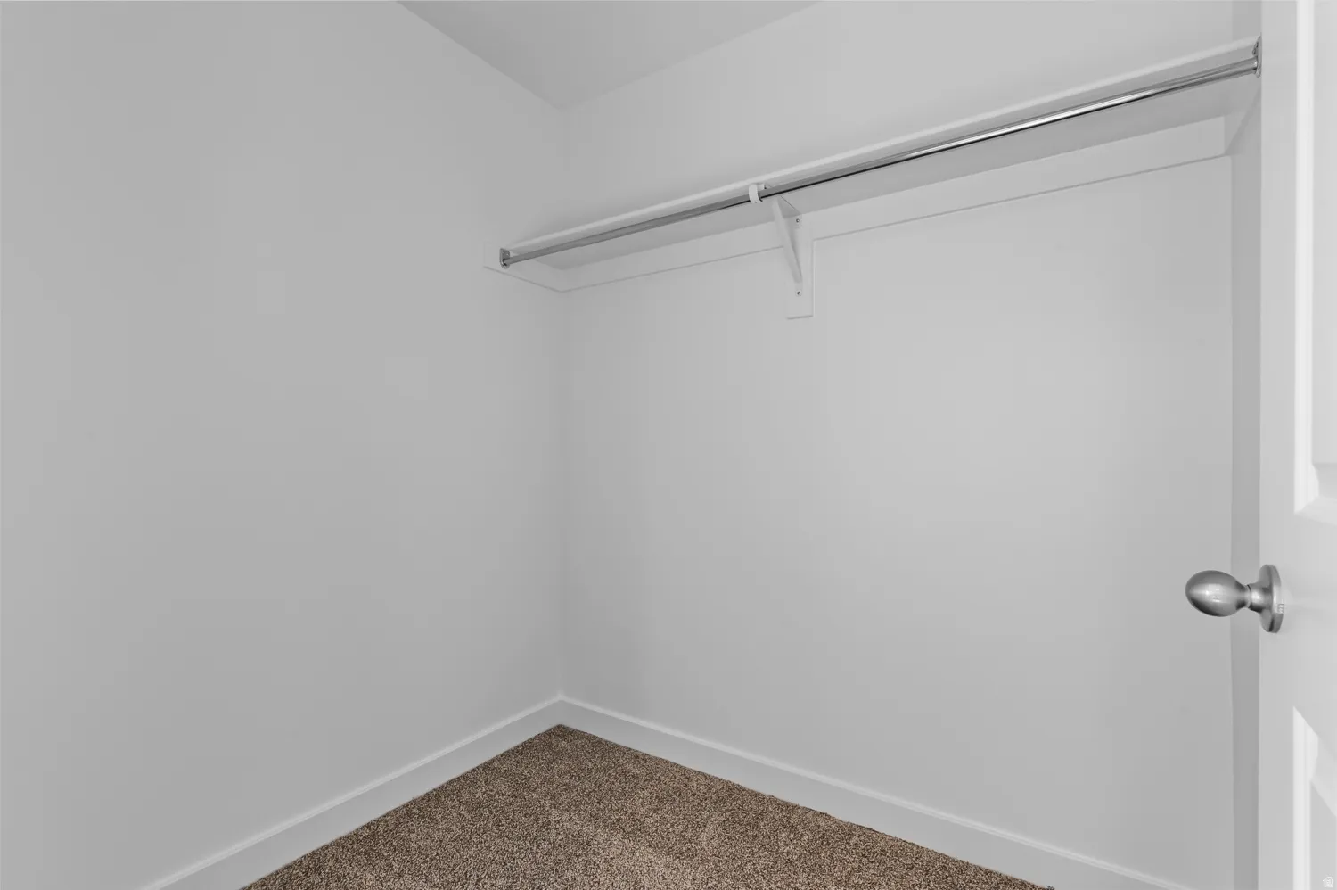 Interior closet featuring a single chrome hanging rod, an integrated shelf, plush carpet flooring, white painted walls, and white baseboards
