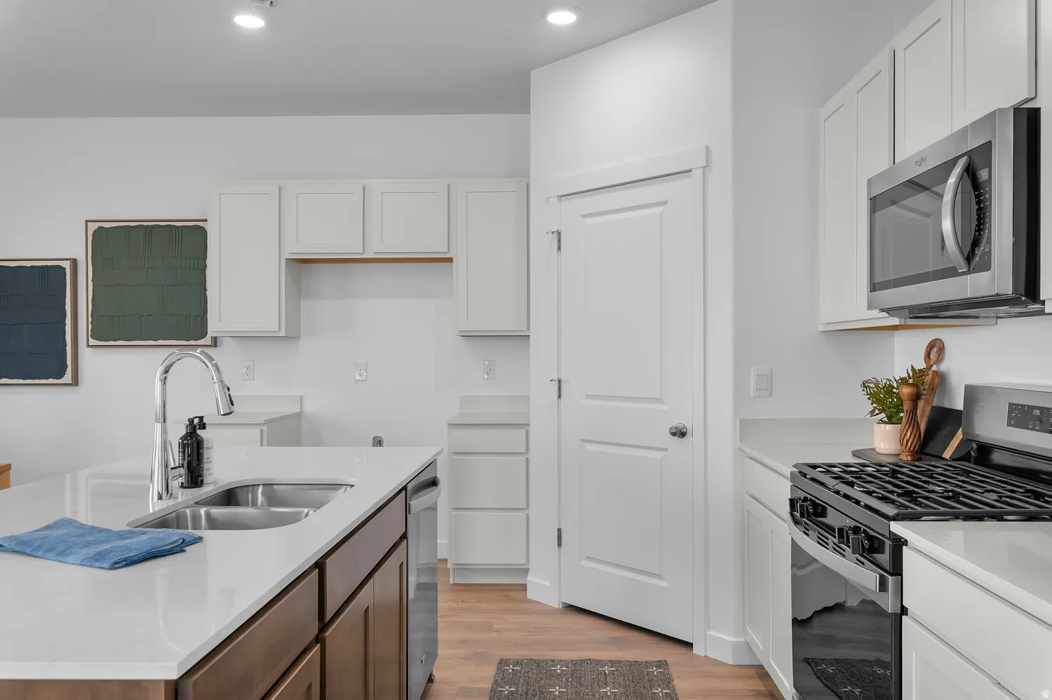 Modern kitchen featuring a stainless steel double basin sink with a high-arc faucet, light-toned countertops, white upper cabinetry, and contrasting wood-finish lower cabinetry on the island