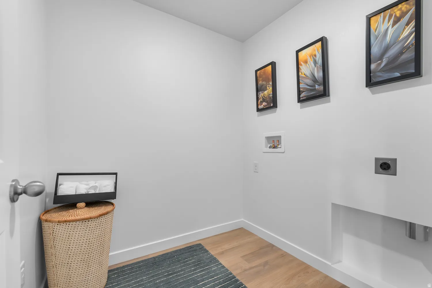 Dedicated laundry area featuring light wood-finish flooring, white walls, and prominent hookups for a washer and dryer