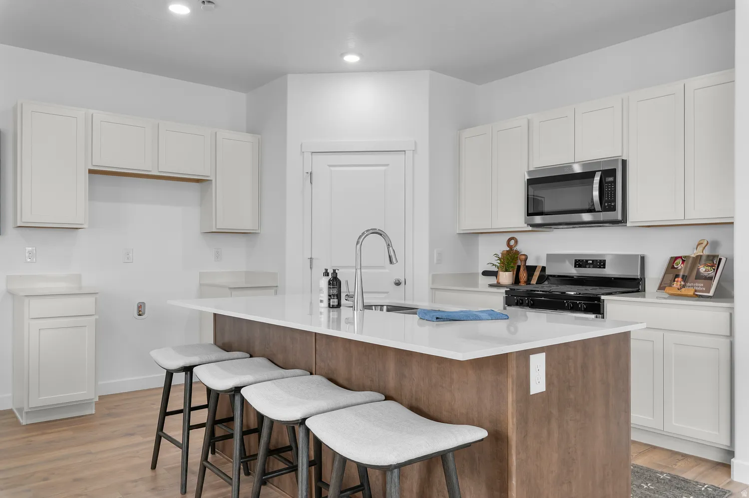 Modern kitchen featuring a large central island with seating, white shaker cabinetry, stainless steel appliances, and wood-finish flooring