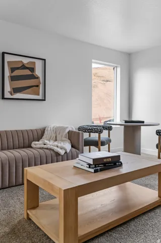 Bright interior space featuring a window with natural light, light-colored carpeting, and a framed abstract wall art piece