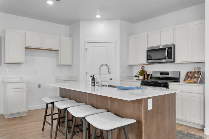 Modern kitchen featuring a large central island with seating, white shaker cabinetry, stainless steel appliances, and wood-finish flooring