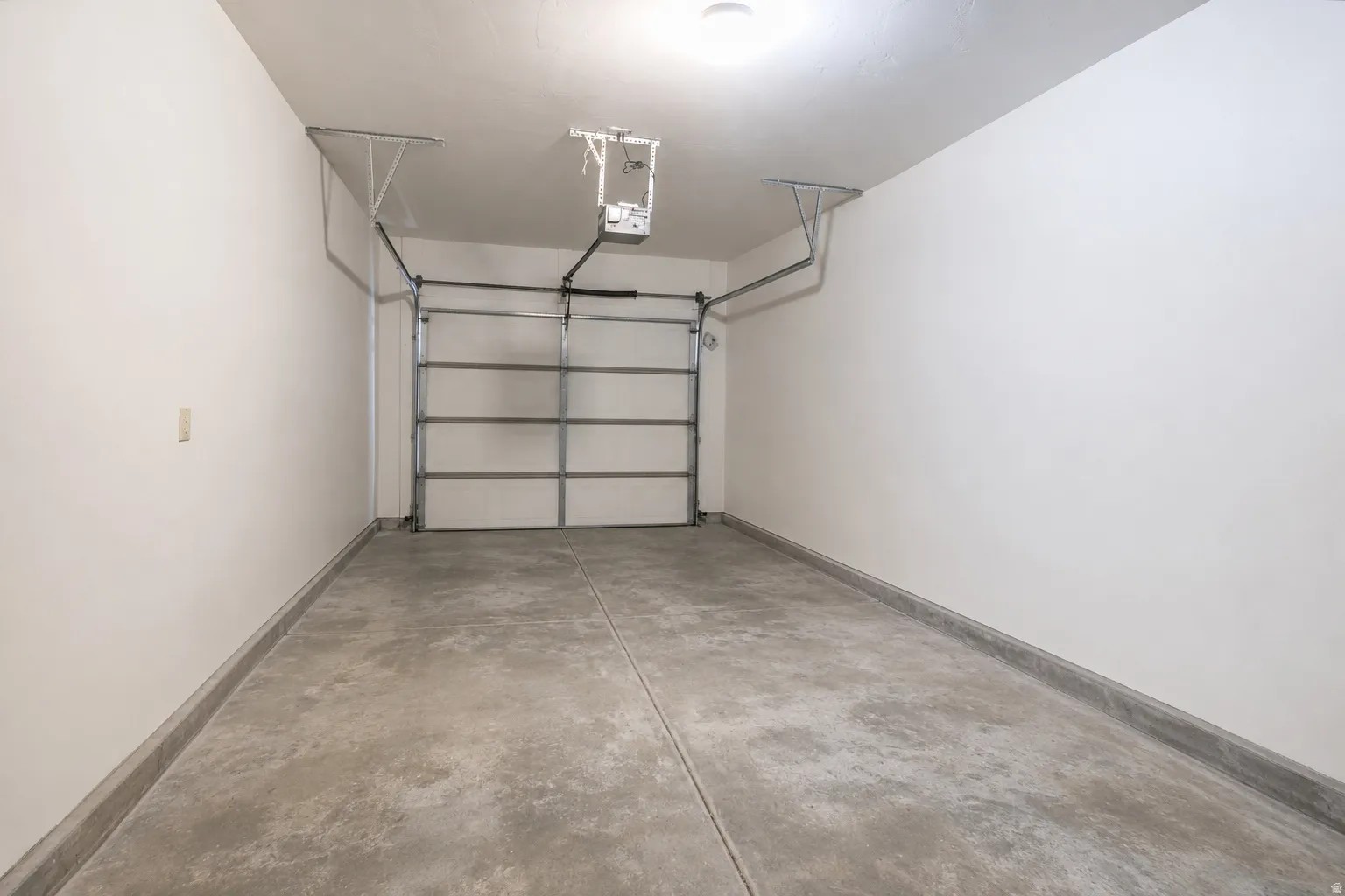 Garage interior featuring a concrete floor, painted white walls, an overhead garage door, and an automatic garage door opener