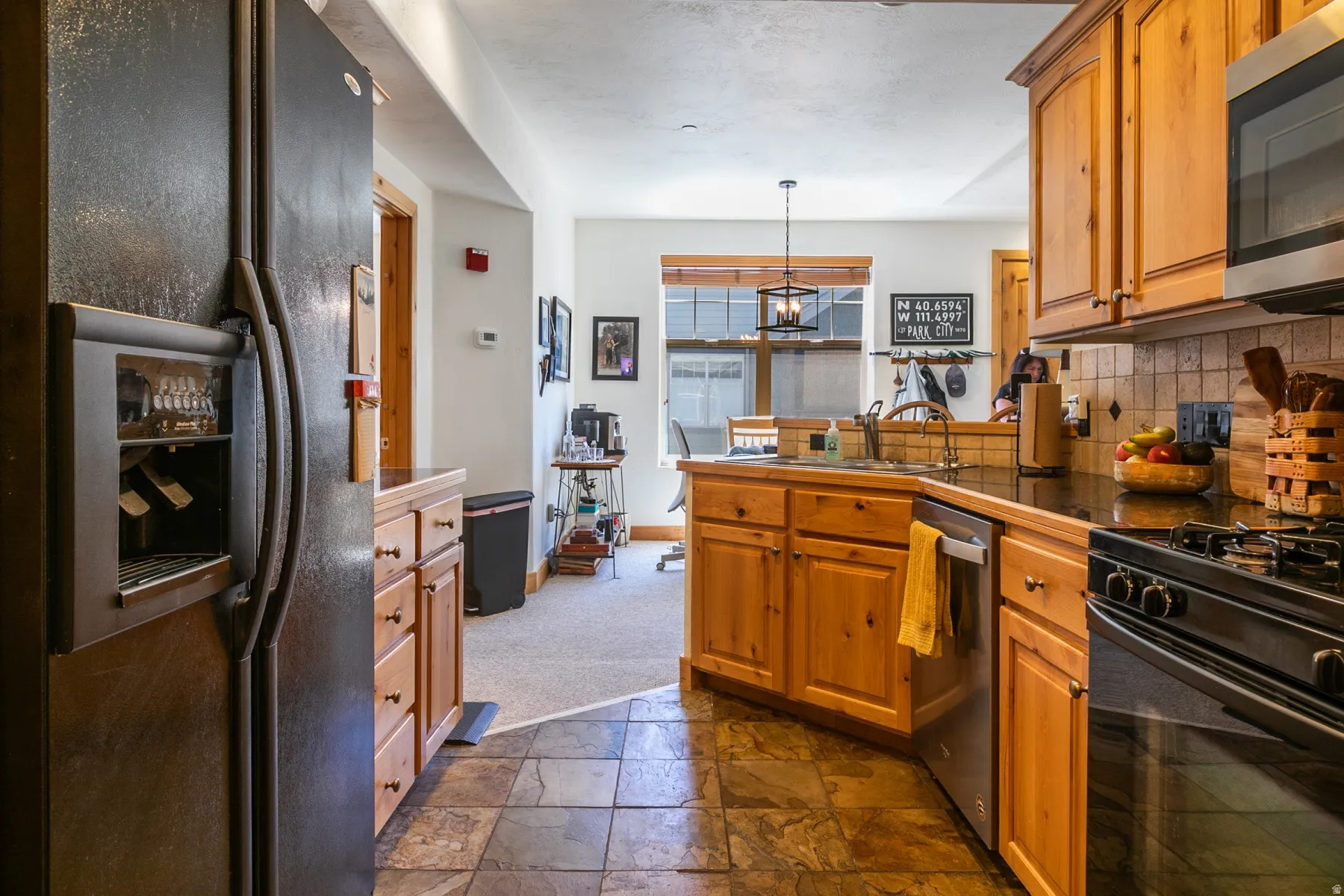 Kitchen featuring rich wood cabinetry, stone-finish flooring, dark countertops, and stainless steel appliances