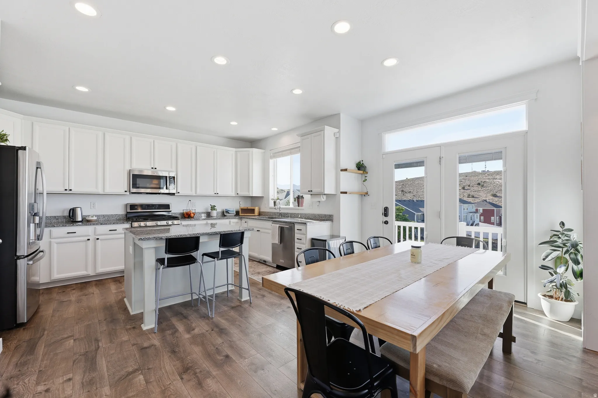 Open-concept kitchen and dining area featuring wood-finish flooring, white cabinetry, a kitchen island with seating, stainless steel appliances, and French doors with an overhead transom window