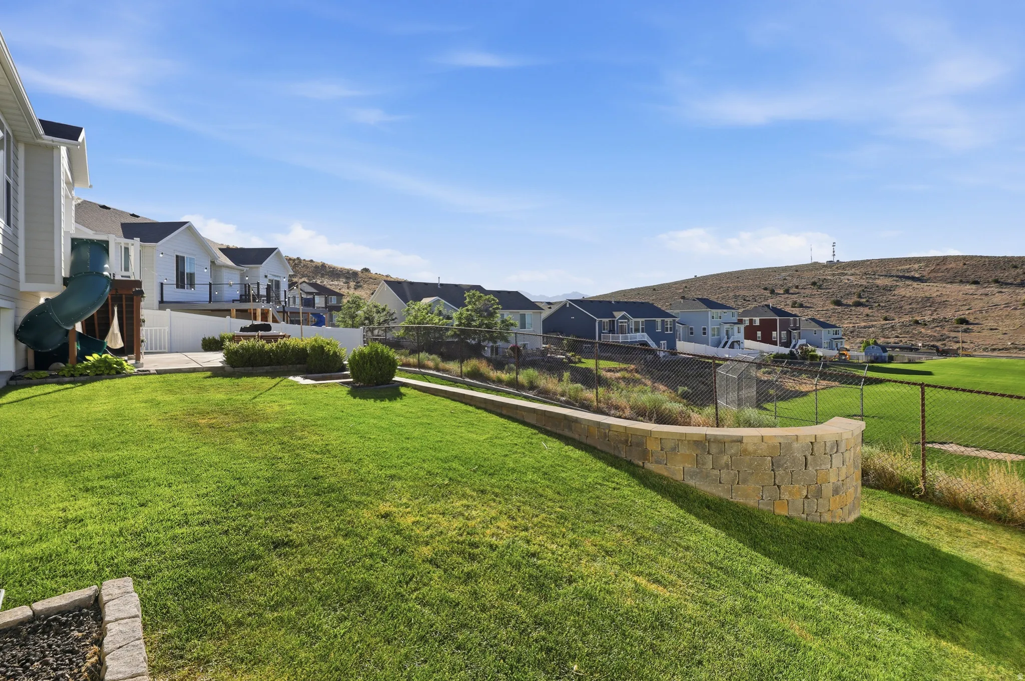 Expansive terraced backyard featuring a stone retaining wall, grassy lawn, and chain-link fencing