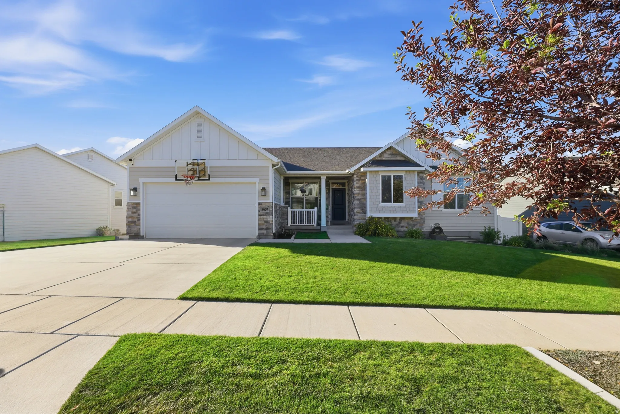 Contemporary ranch-style home featuring a stone and siding exterior, a front-facing attached garage, a covered front porch, and a concrete driveway