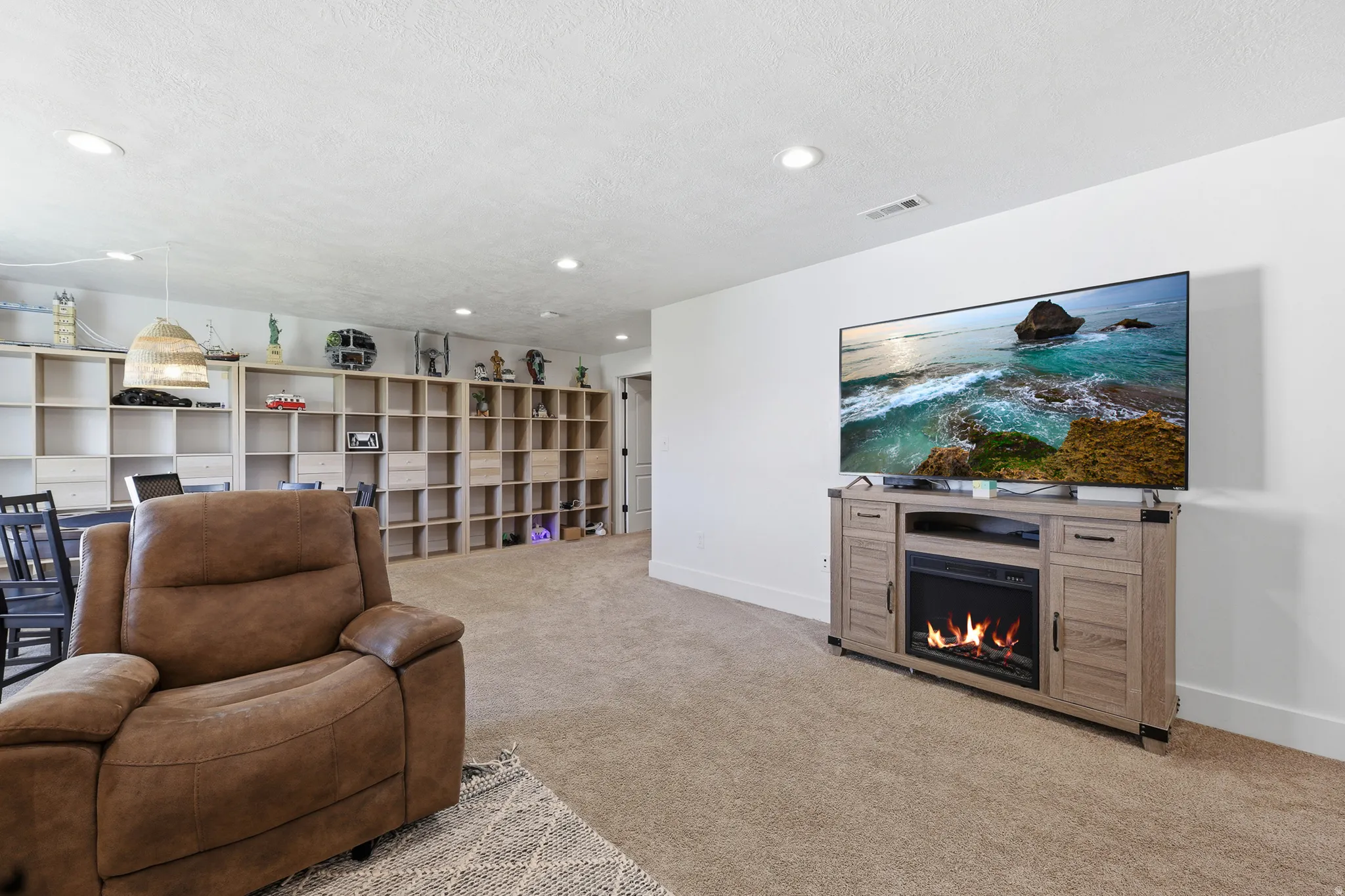 Spacious room featuring neutral carpeting, recessed lighting, built-in shelving, and a media console with an integrated fireplace