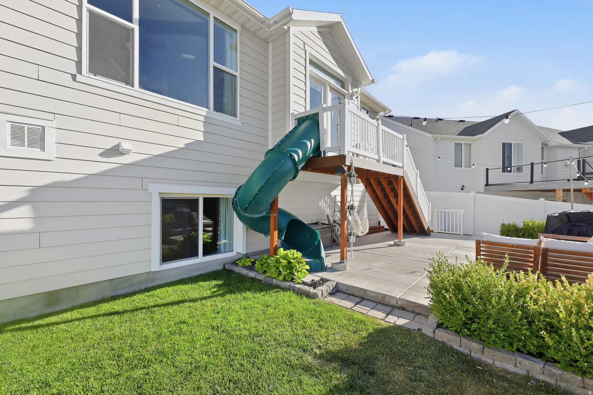 Rear exterior featuring a concrete patio, wood deck with white railing, and a green slide