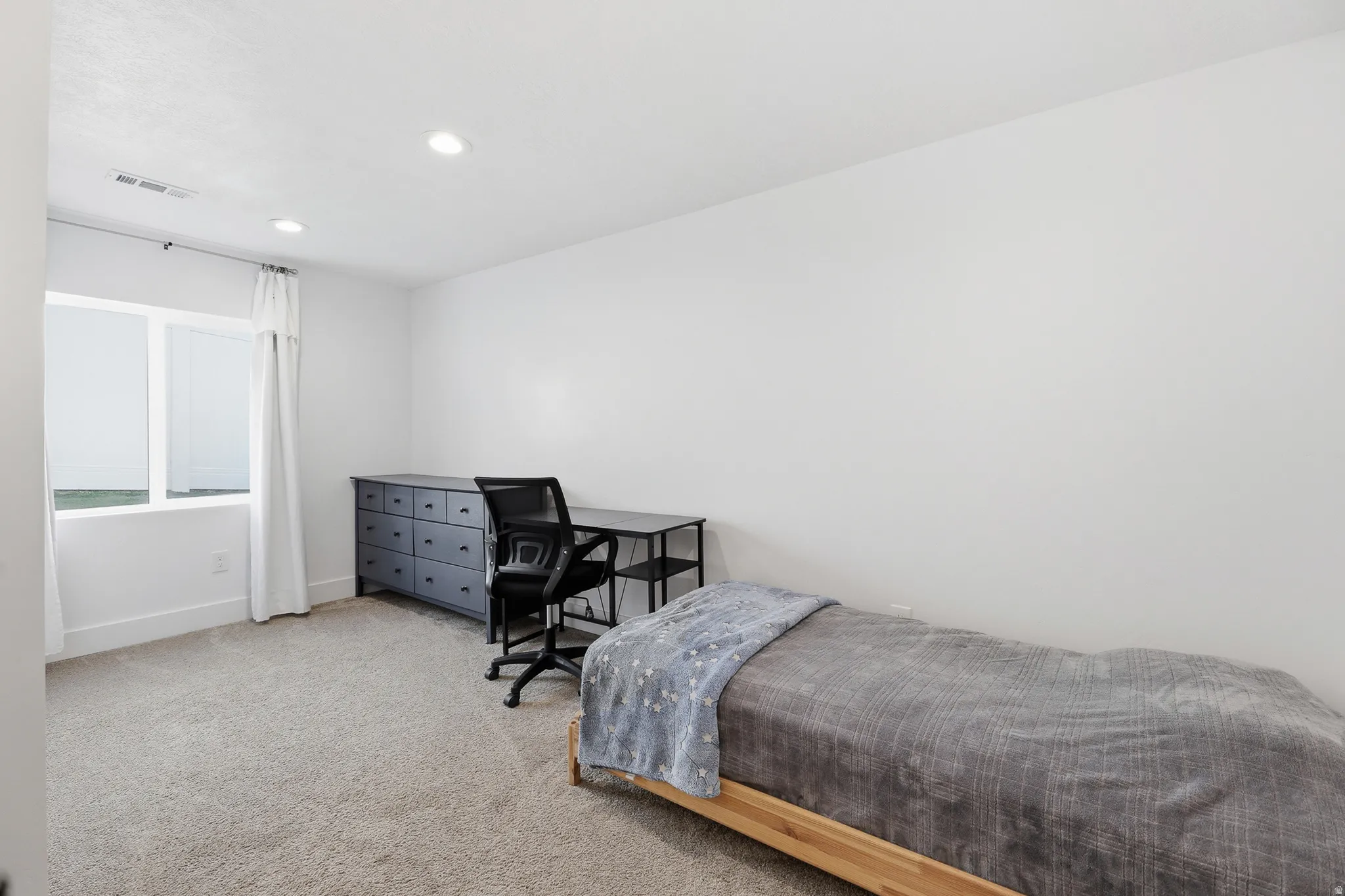 Light-filled room featuring neutral carpeting, white walls, recessed ceiling lighting, and a large window with white trim