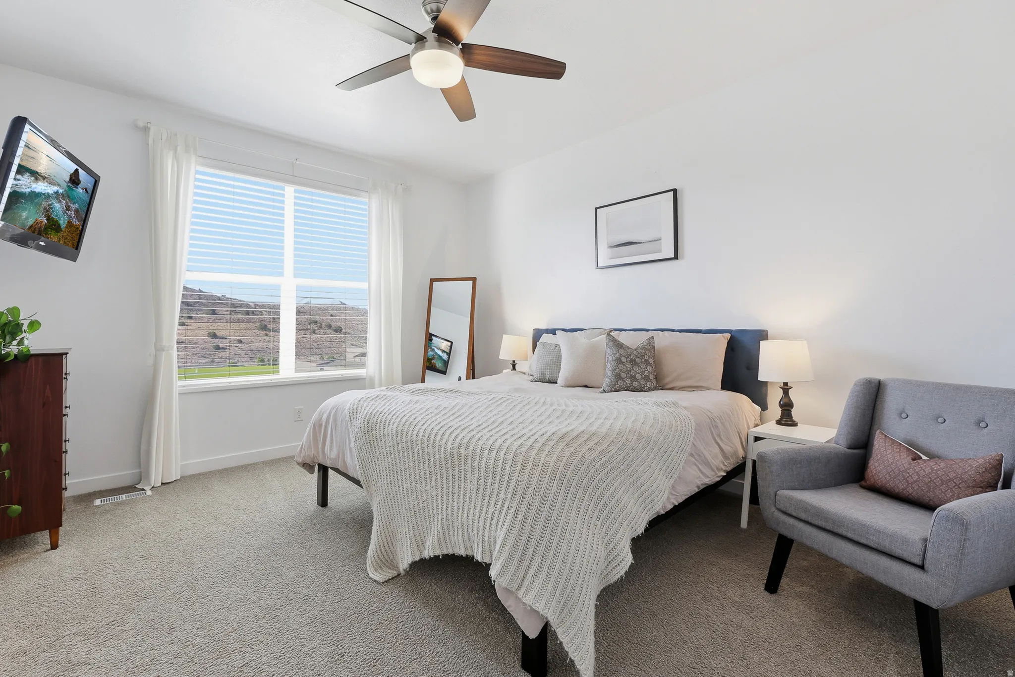 Bedroom featuring a large window, neutral carpeting, a ceiling fan with integrated lighting, and white walls