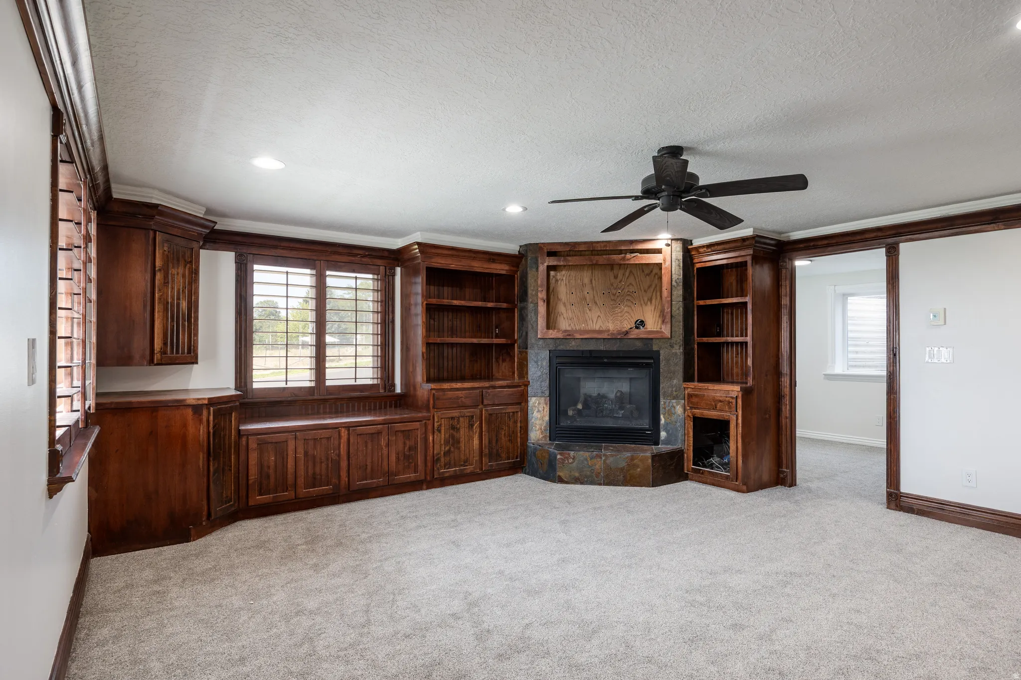 Built-in cabinetry and shelving, corner fireplace with stone surround, ceiling fan, and window shutters