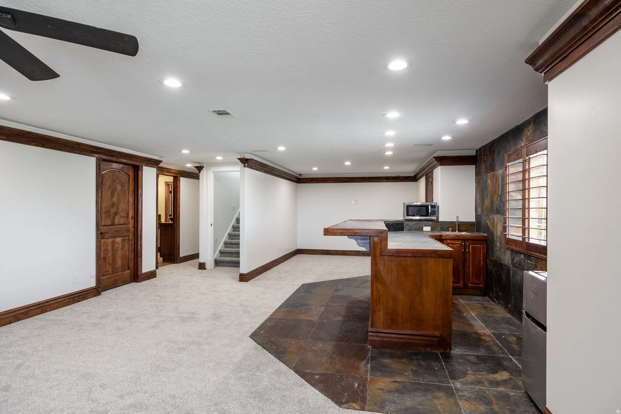 Spacious room with recessed lighting, wood-finish trim, and a built-in wet bar featuring a microwave, sink, and under-counter refrigerator
