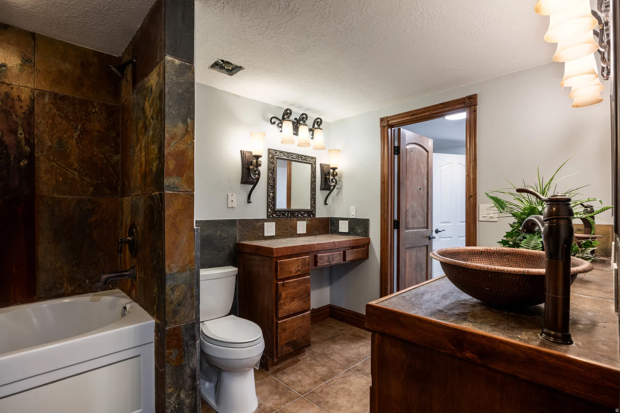 Stone-tiled shower with a white bathtub, wood vanity with a basin sink, and a built-in makeup counter