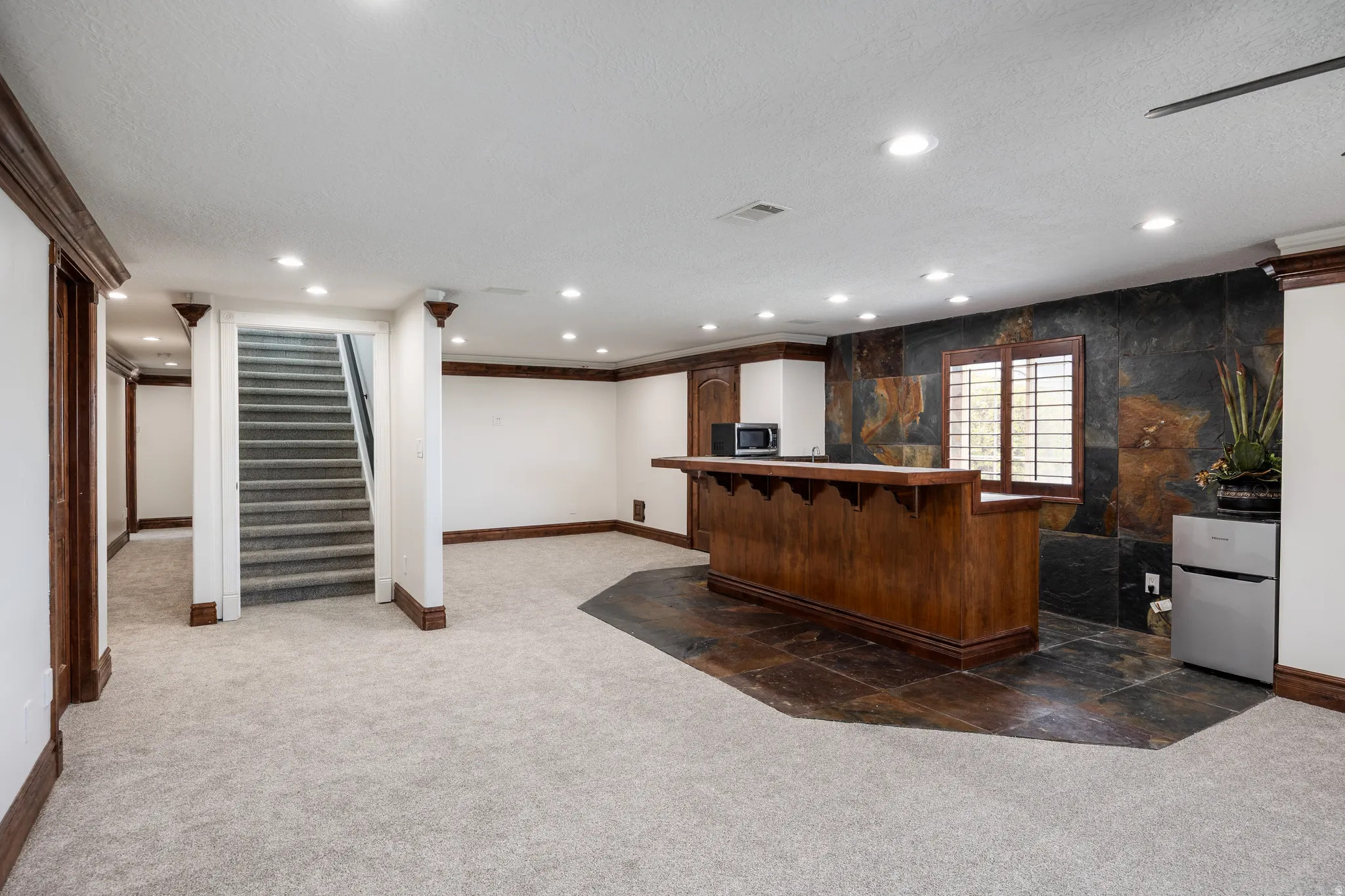 Spacious room featuring a built-in wood-finish bar, recessed lighting, and a slate-tiled accent wall